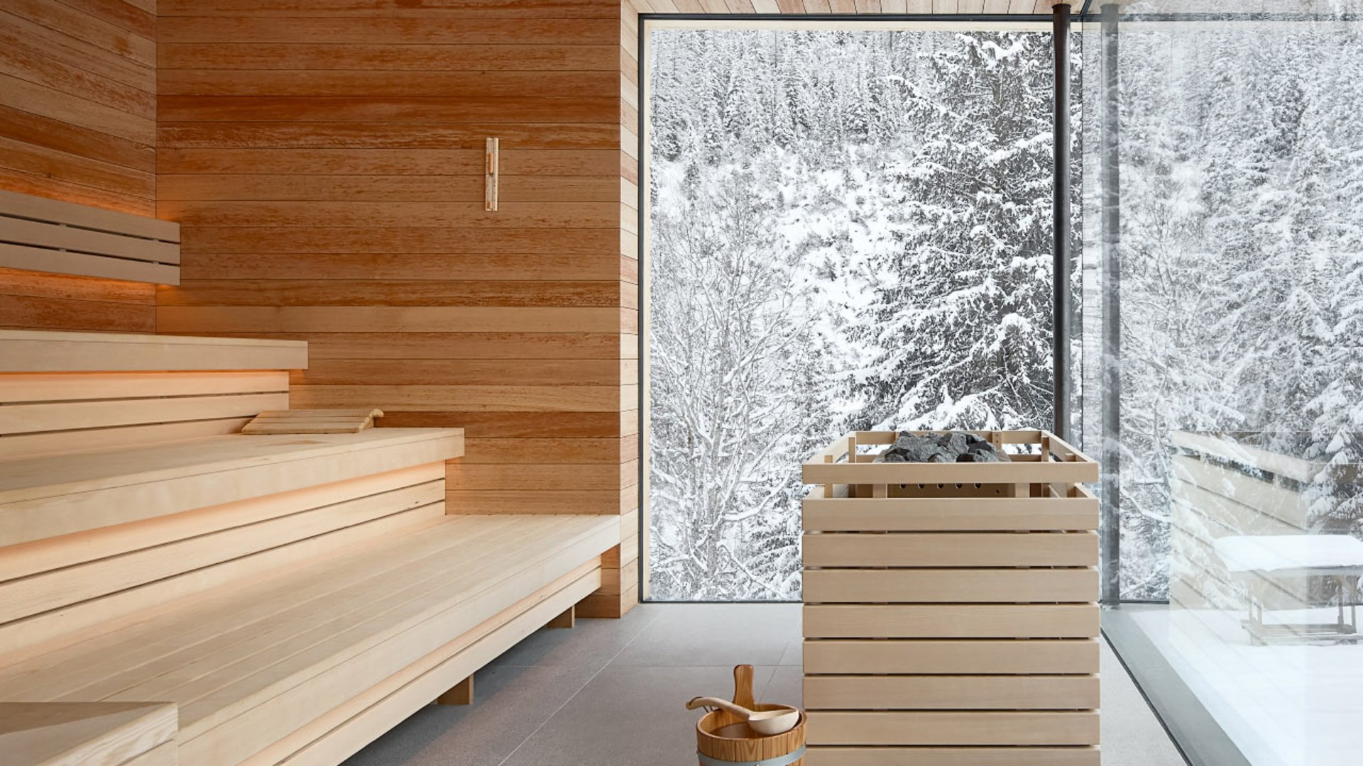 Cozy sauna with large glass front at Hotel Bella Vista, revealing views of the snow-covered forest landscape and creating an atmosphere of tranquility.