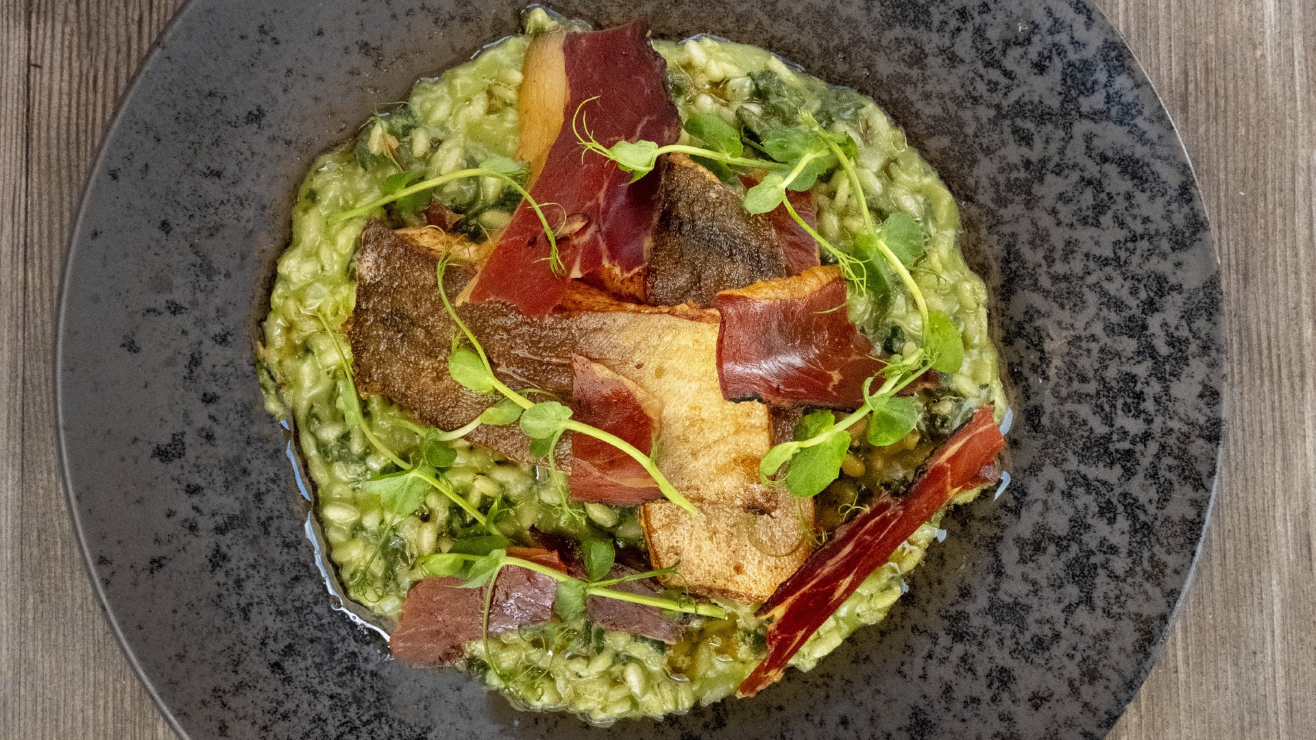 Gourmetgericht von Hotel Bella Vista, kreativ präsentiertes Risotto mit knusprigen Entenbruststreifen auf rustikalem Schieferplattenteller.