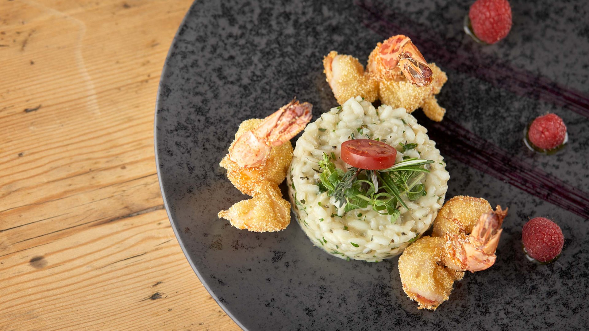 Gourmet dish at Hotel Bella Vista, delicately plated risotto with crispy prawns and fresh berries on a black plate for a culinary experience.
