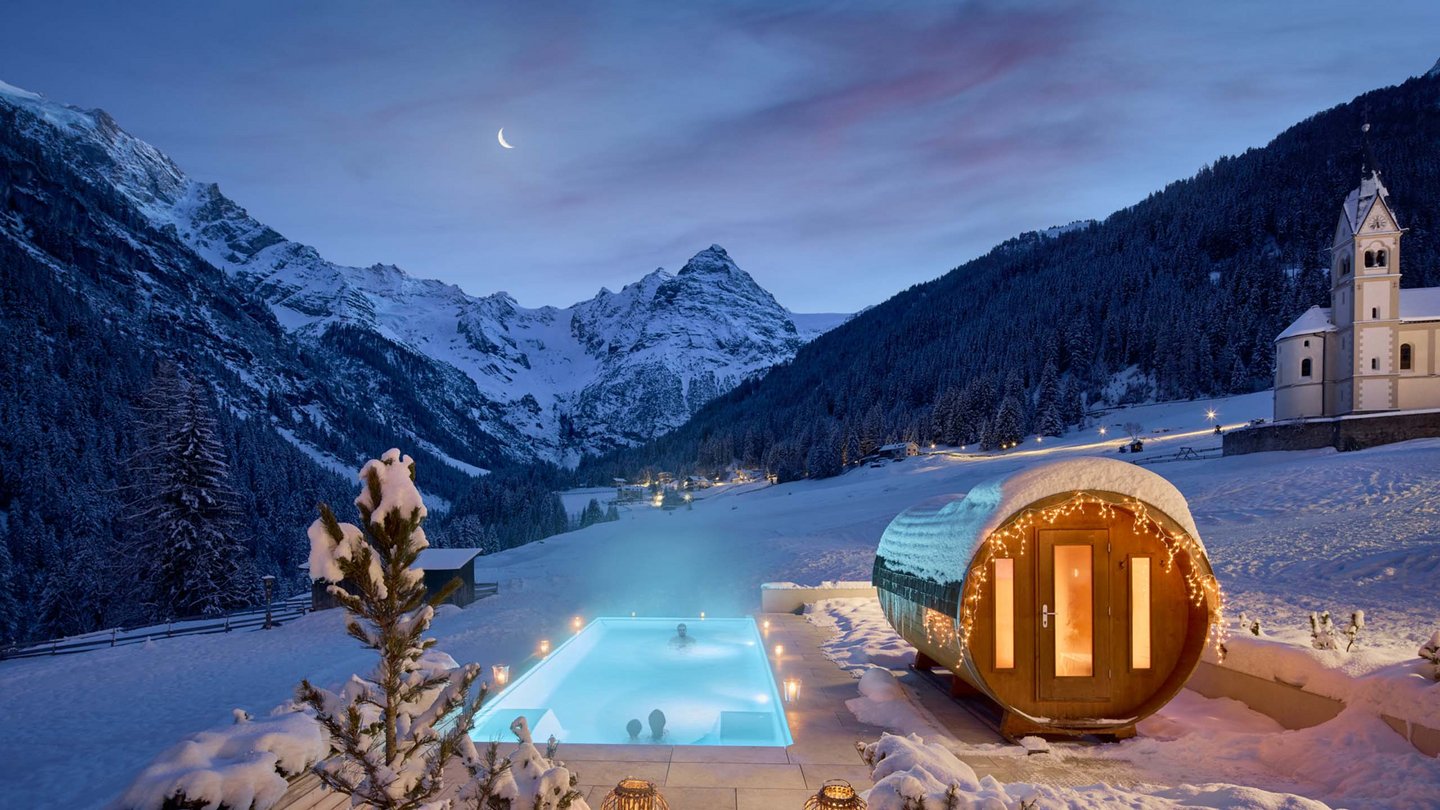 Winterzauber am beheizten Außenpool des Hotel Bella Vista mit Blick auf schneebedeckte Berge und klaren Sternenhimmel.
