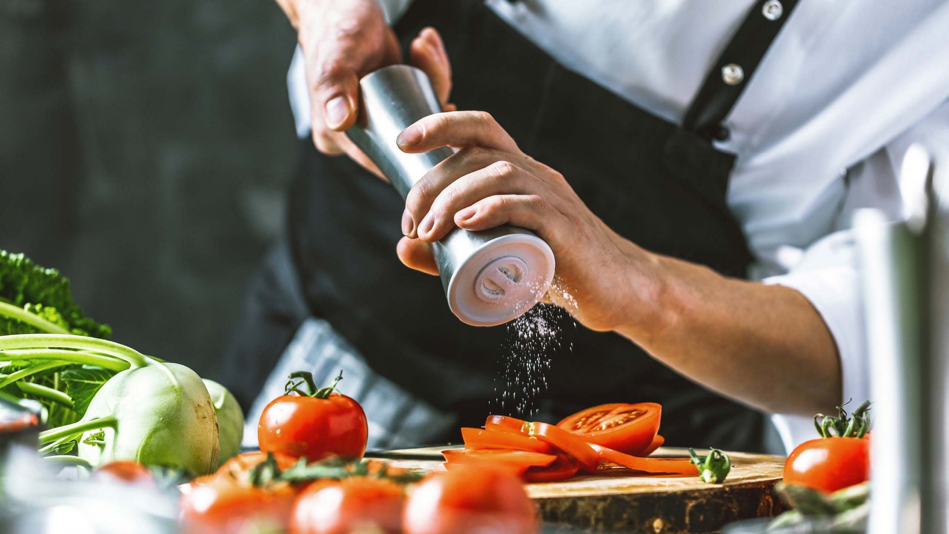 Ein Küchenchef im Hotel Bella Vista würzt sorgfältig frische Zutaten, ein Einblick in die kulinarische Hingabe und Qualität der Hotelküche.