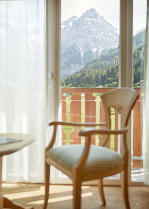 Relaxing seating area with a chair and table by the window at Hotel Bella Vista, featuring inspiring views of the majestic Alps.