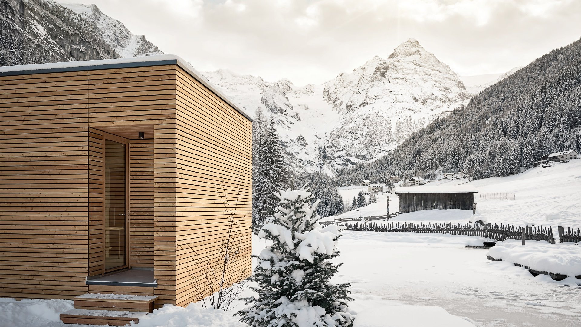 Outdoor sauna with a unique wooden facade set against a snowy mountain landscape, snowflakes visibly falling.