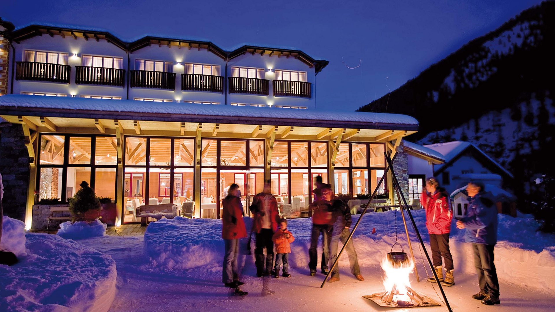 Joyful guests enjoy warming mulled wine in the winter ambiance by the fireplace at Hotel Bella Vista, South Tyrol.